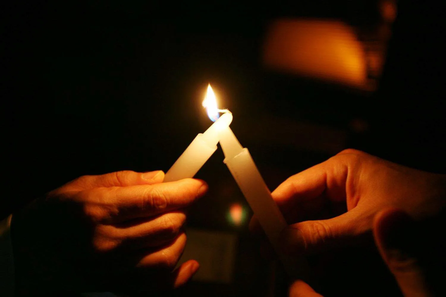 one candle being lit by another candle being held in hands