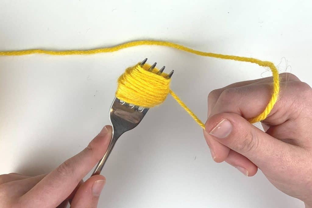 Yarn wrapped around a fork for a pom-pom