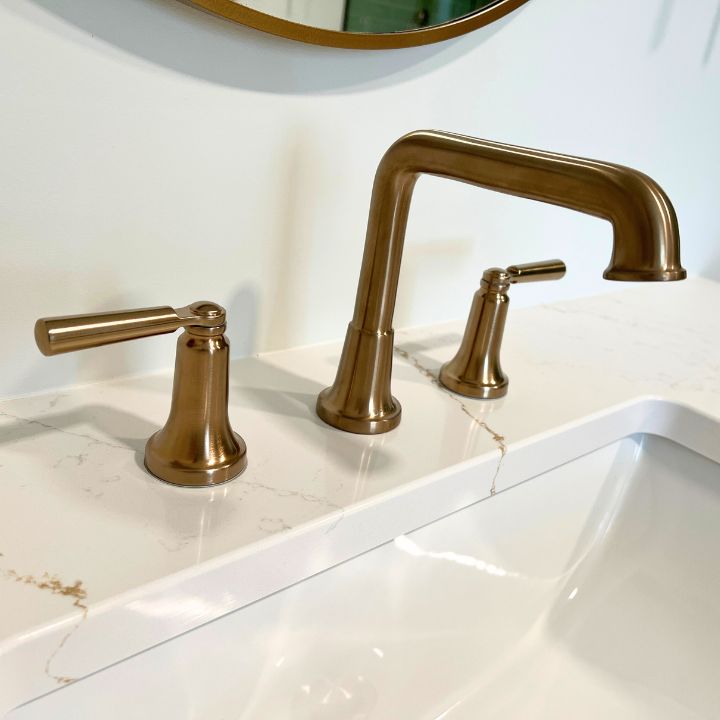 a delta champagne bronze bathroom faucet installed in quartz countertops